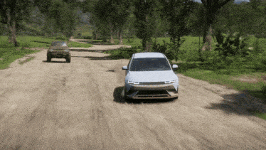 a white car is driving down a dirt road next to a brown suv