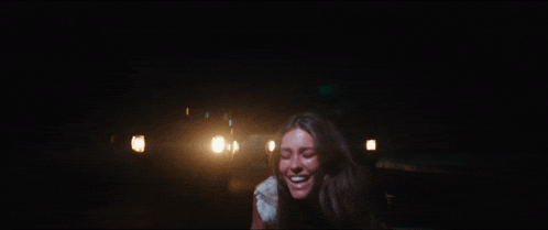 a woman is screaming in the dark with a car behind her