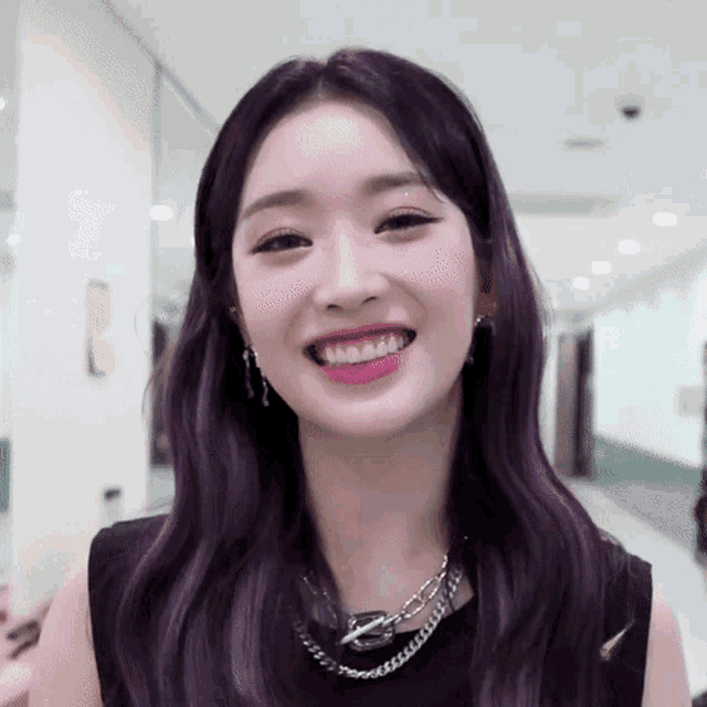a woman with purple hair is smiling and wearing a necklace and earrings