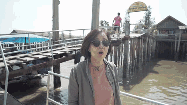a woman wearing sunglasses is standing on a dock near a sign that says " bangkok seafood "
