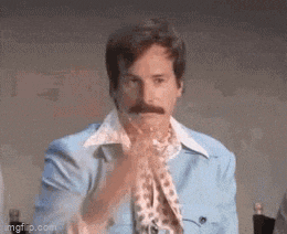 a man with a mustache is wearing a blue jacket and a scarf and is clapping his hands .