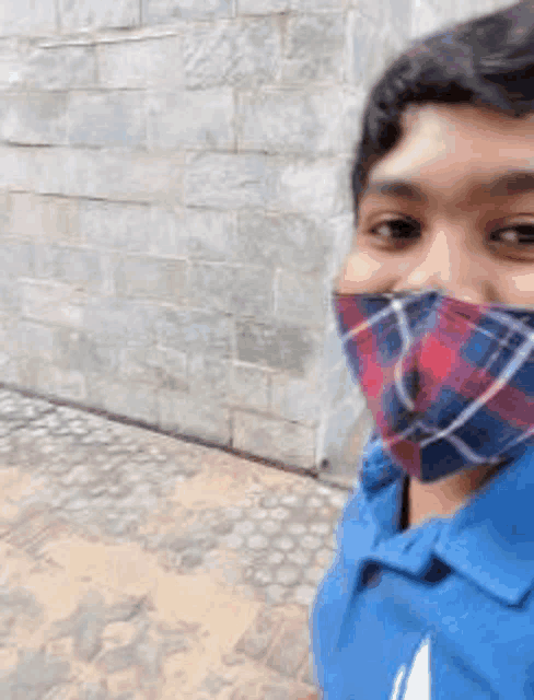 a man wearing a plaid mask is standing in front of a stone wall .