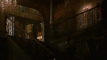 a dinosaur is standing on a set of stairs in a dark room with a chandelier