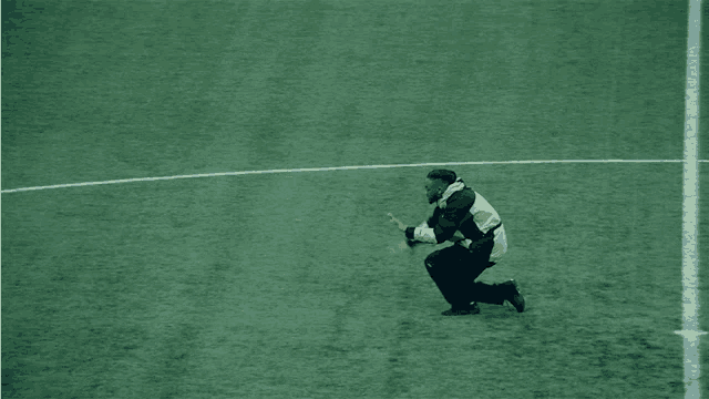 a man in a yellow and black jacket is squatting down on a soccer field