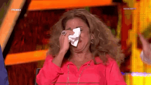 a woman in a pink shirt is covering her face with a napkin while sitting on a stage .