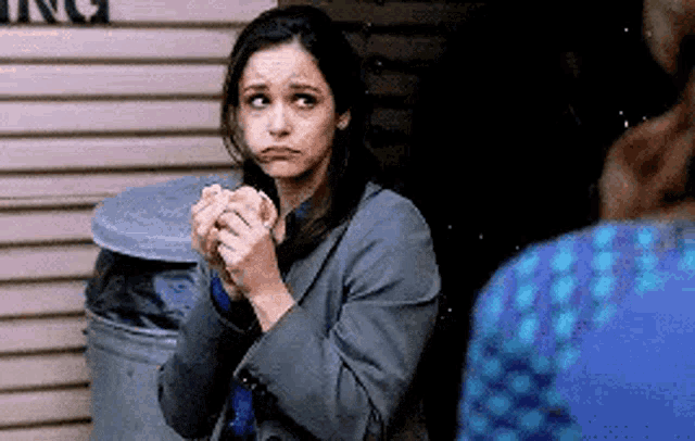 a woman in a suit is holding a hamburger in her hands and making a face .