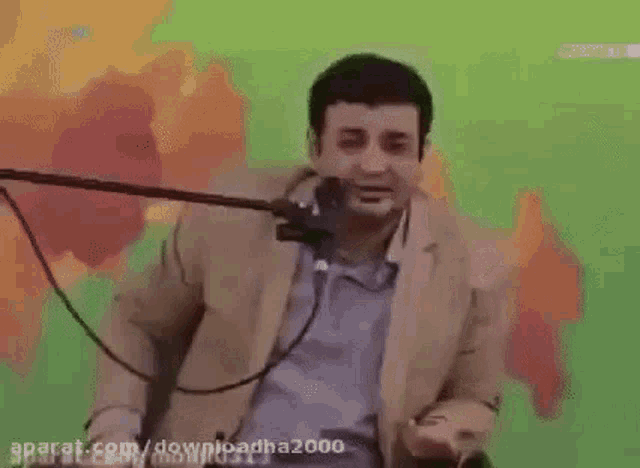 a man in a suit is talking into a microphone while sitting in front of a green screen .
