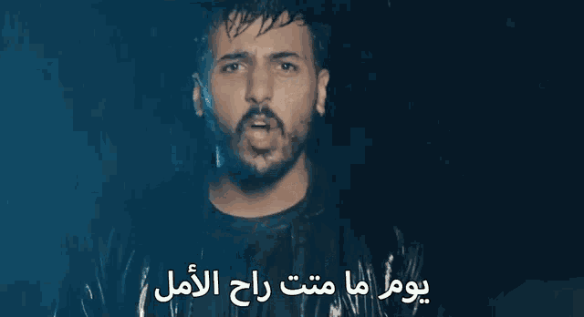 a man with a beard is standing in the rain with arabic writing on the bottom