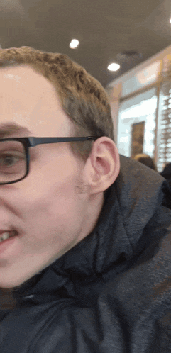 a man wearing glasses and a black jacket smiles