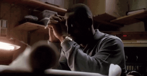a man is sitting at a desk in a dark room with his hands on his face .