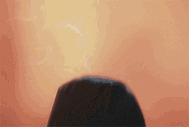a blurry picture of a woman 's face with a hood on against an orange background .