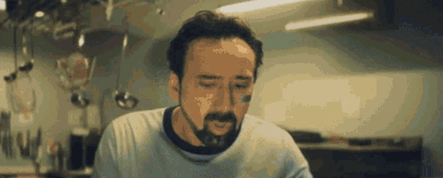 a man with a beard is standing in a kitchen with a spoon on his forehead .