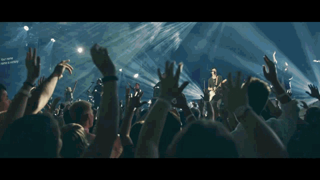 a crowd of people at a concert with their hands in the air and a sign that says your name is victory