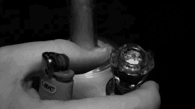 a person holding a bic lighter next to a glass bong