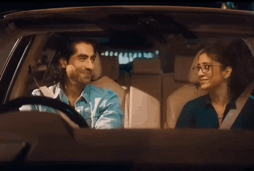 a man and a woman are sitting in a car looking at each other and smiling .