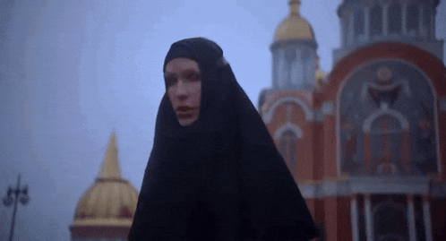 a woman in a black head scarf stands in front of a church