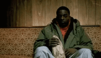 a man in a green jacket is sitting on a couch holding a bag of popcorn .