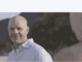 a bald man in a white shirt is smiling and looking at another man .