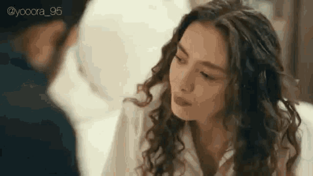 a woman with curly hair is sitting next to a man on a bed and looking at him .