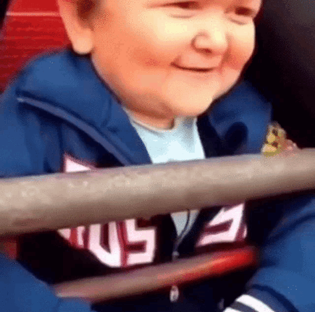 a young boy in a blue jacket is smiling while sitting in a chair .