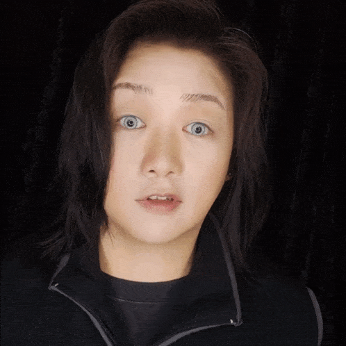 a woman with a surprised look on her face is wearing a jacket with a zipper that says ' g '