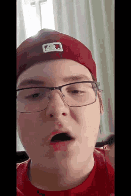 a young man wearing glasses and a red baseball cap