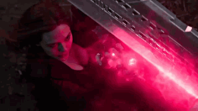 scarlet witch is holding a red light in her hand while standing under a bridge .