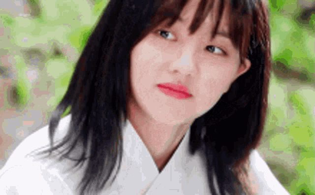 a close up of a woman 's face with a white shirt on looking at the camera .