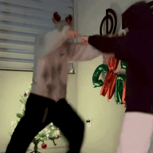 two people are fighting in front of a christmas tree and balloons that say christmas