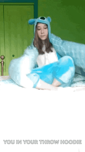 a girl is laying on a bed wearing a throw hoodie .