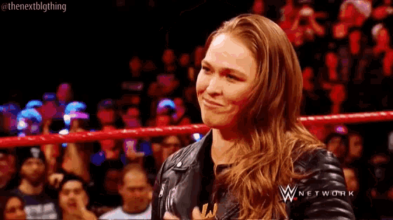 a woman is standing in a wrestling ring with a crowd watching .