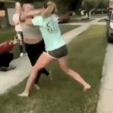 two women are fighting on a sidewalk on a street .