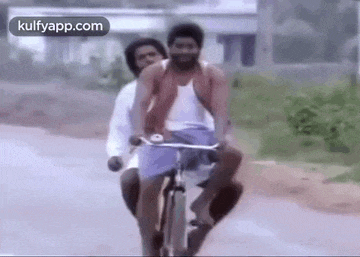 two men are riding a bike on a road .
