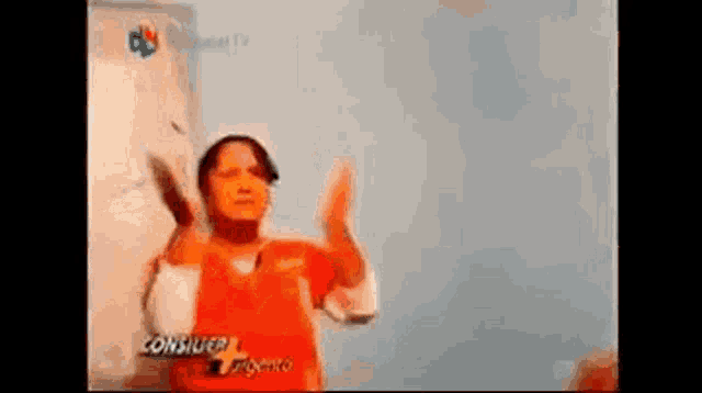 a woman in an orange shirt is standing in front of a blue wall with her arms outstretched .