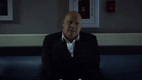a man in a suit sits in front of a fire extinguisher on the wall