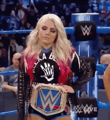 a woman is standing in a wrestling ring holding a wrestling belt .