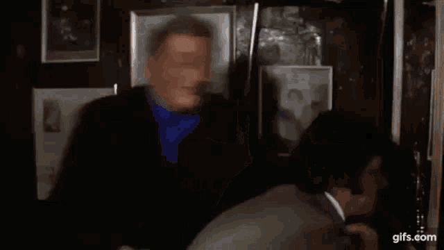 a man in a suit and blue shirt is hugging another man in a room with pictures on the wall .