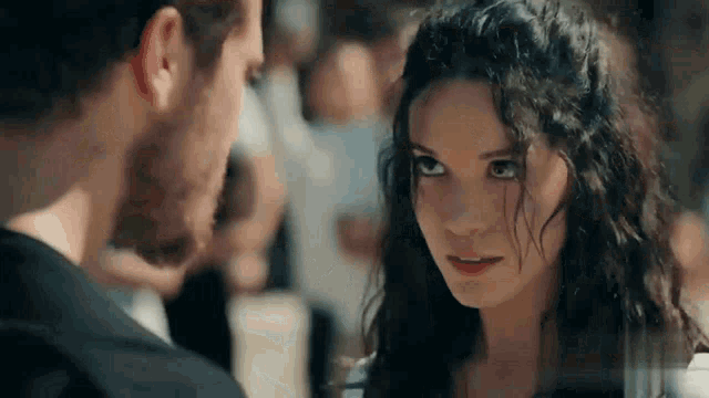 a man and a woman are looking at each other . the woman has curly hair and the man has a beard .