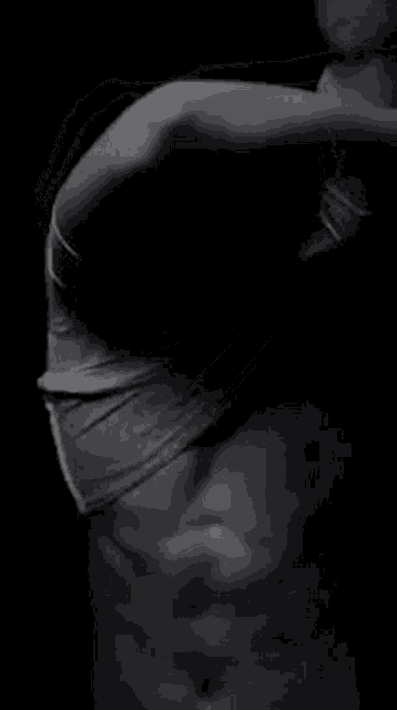 it is a black and white photo of a man taking off his shirt .