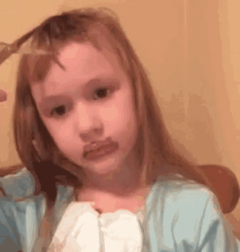 a little girl is cutting her hair with a pair of scissors and making a sad face .