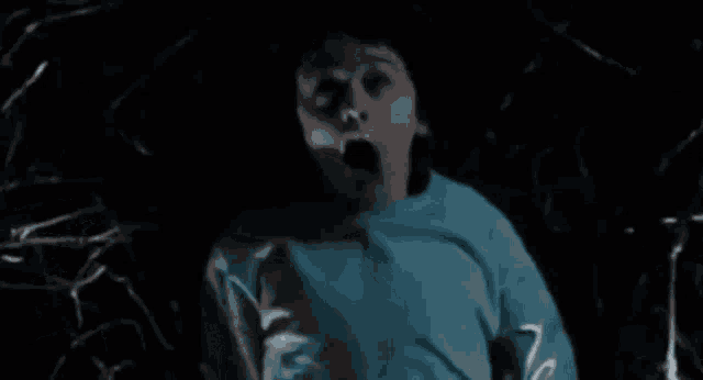 a person in a blue shirt is screaming in the dark .