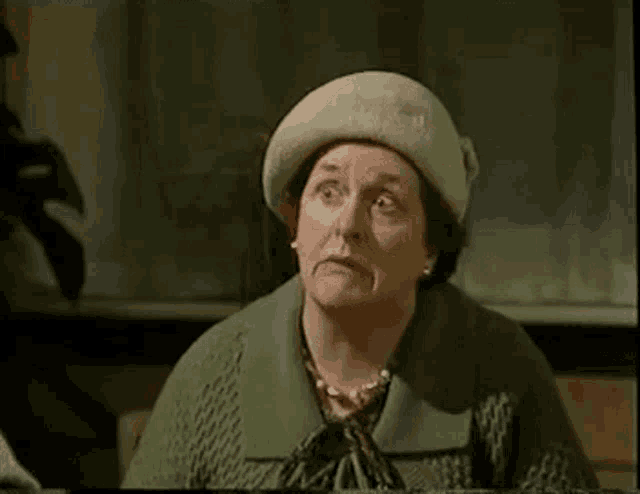 an elderly woman wearing a white hat and a green sweater is sitting at a table .