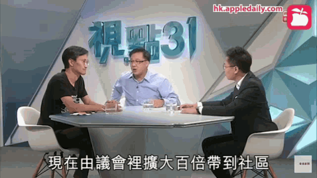 three men are sitting at a table in front of a screen that says hk.appledaily.com