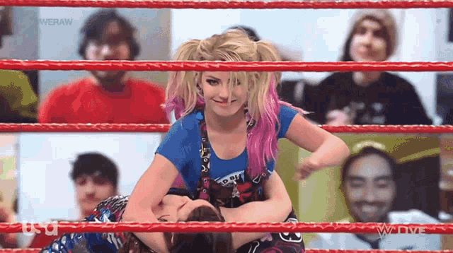 a woman in a blue shirt is wrestling another woman in a red ring .