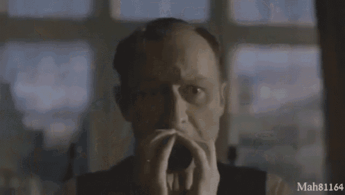 a man with his hands folded in front of a window with mah81184 in the corner