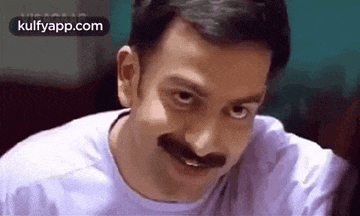 a man with a mustache is smiling and looking at the camera while wearing a white shirt .