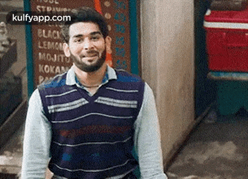 a man with a beard is standing in front of a sign that says ' mojito ' on it .