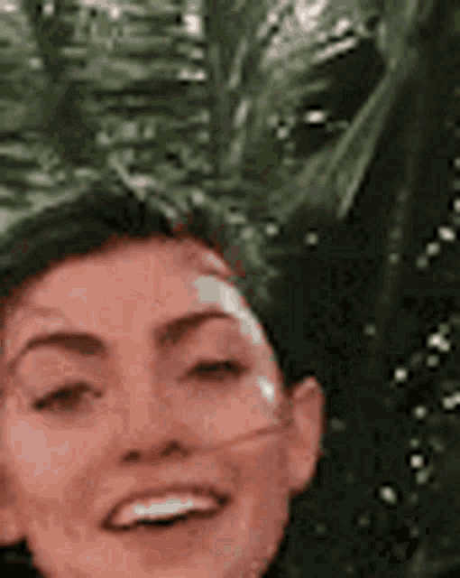 a woman is smiling while standing in front of a palm tree .