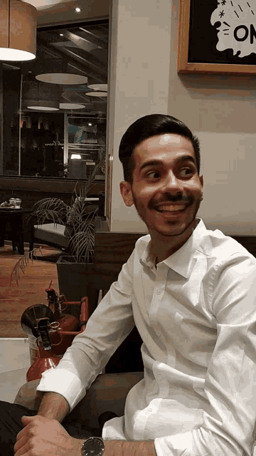 a man in a white shirt is smiling in front of a sign that says " on "