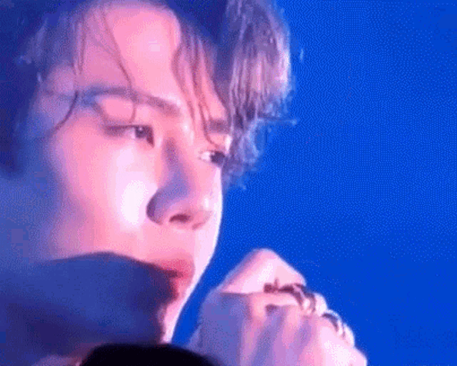 a close up of a man 's face against a blue background while singing into a microphone .